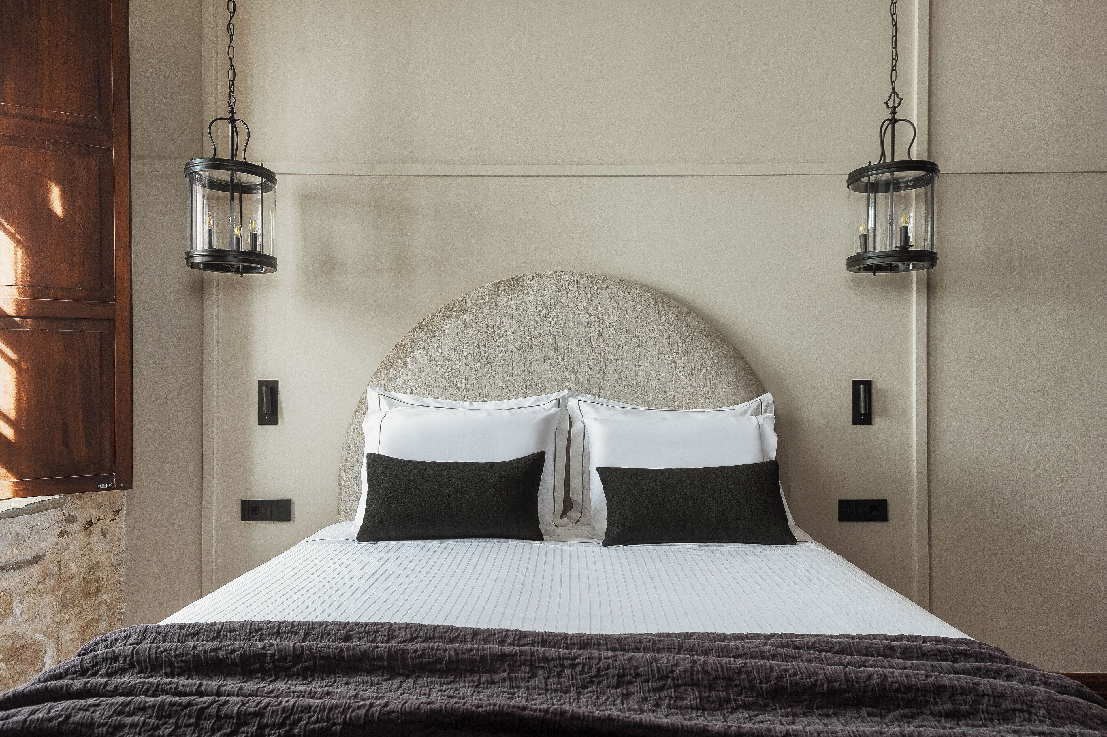 A neatly made bed with a headboard, two bedside lamps, and a dark throw blanket.