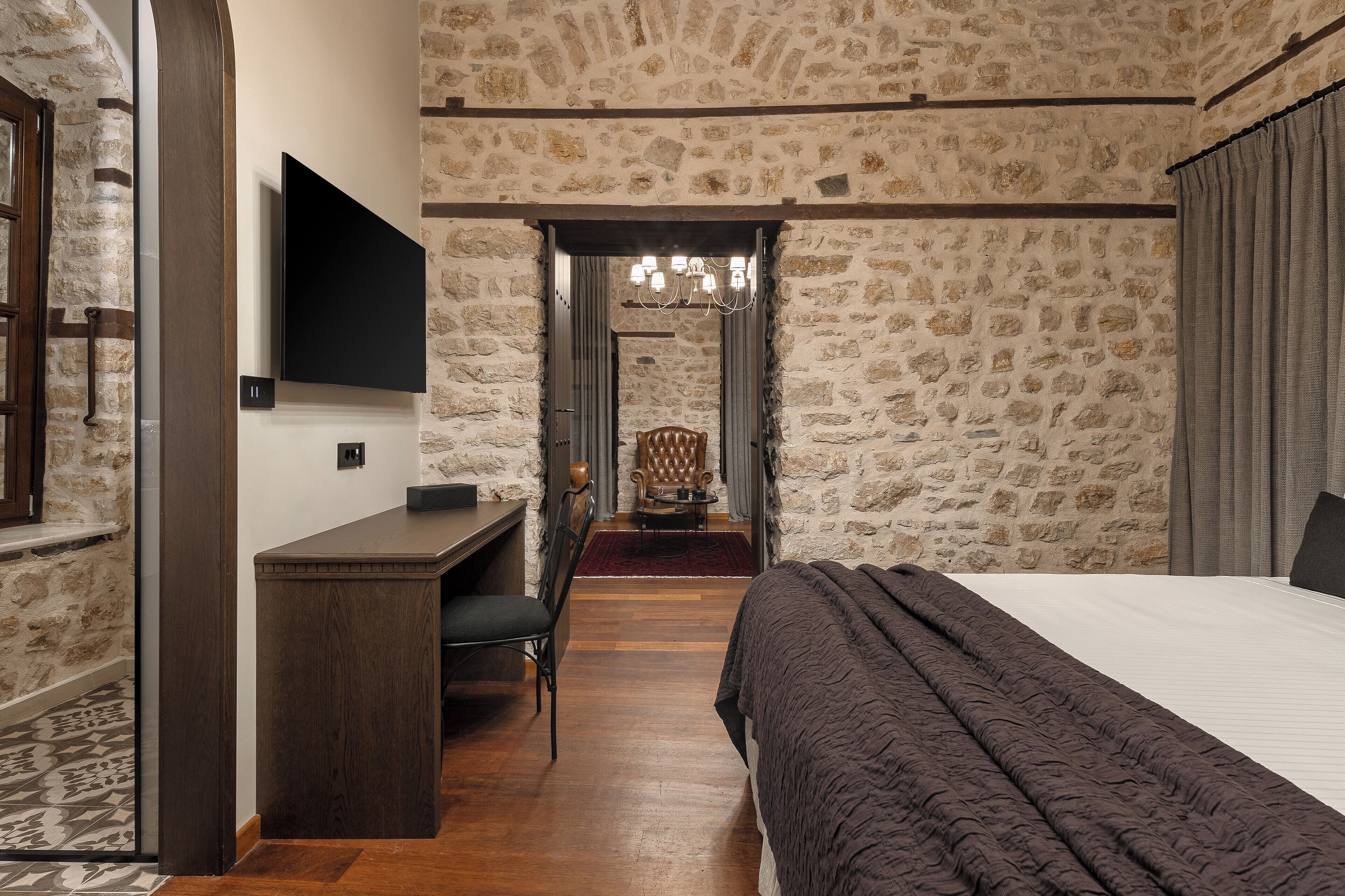 A bedroom with a stone wall, a bed, a desk, and a chair.