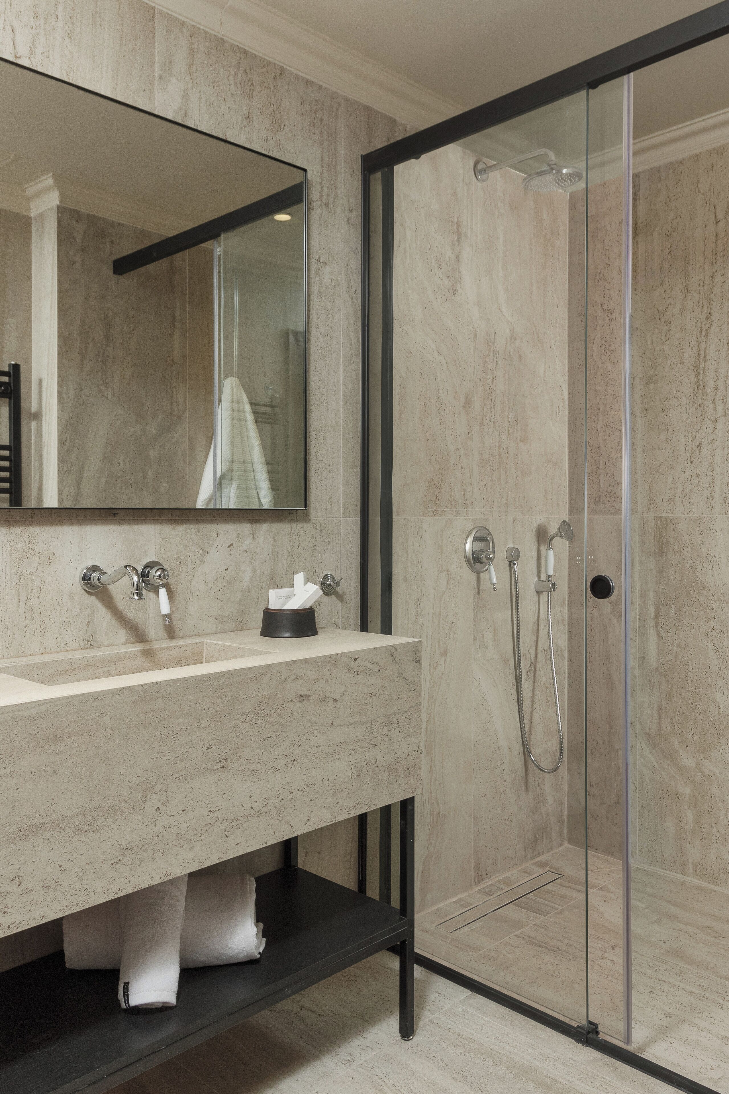 A modern bathroom with a glass-enclosed shower, a large mirror, and a vanity with a towel rack.