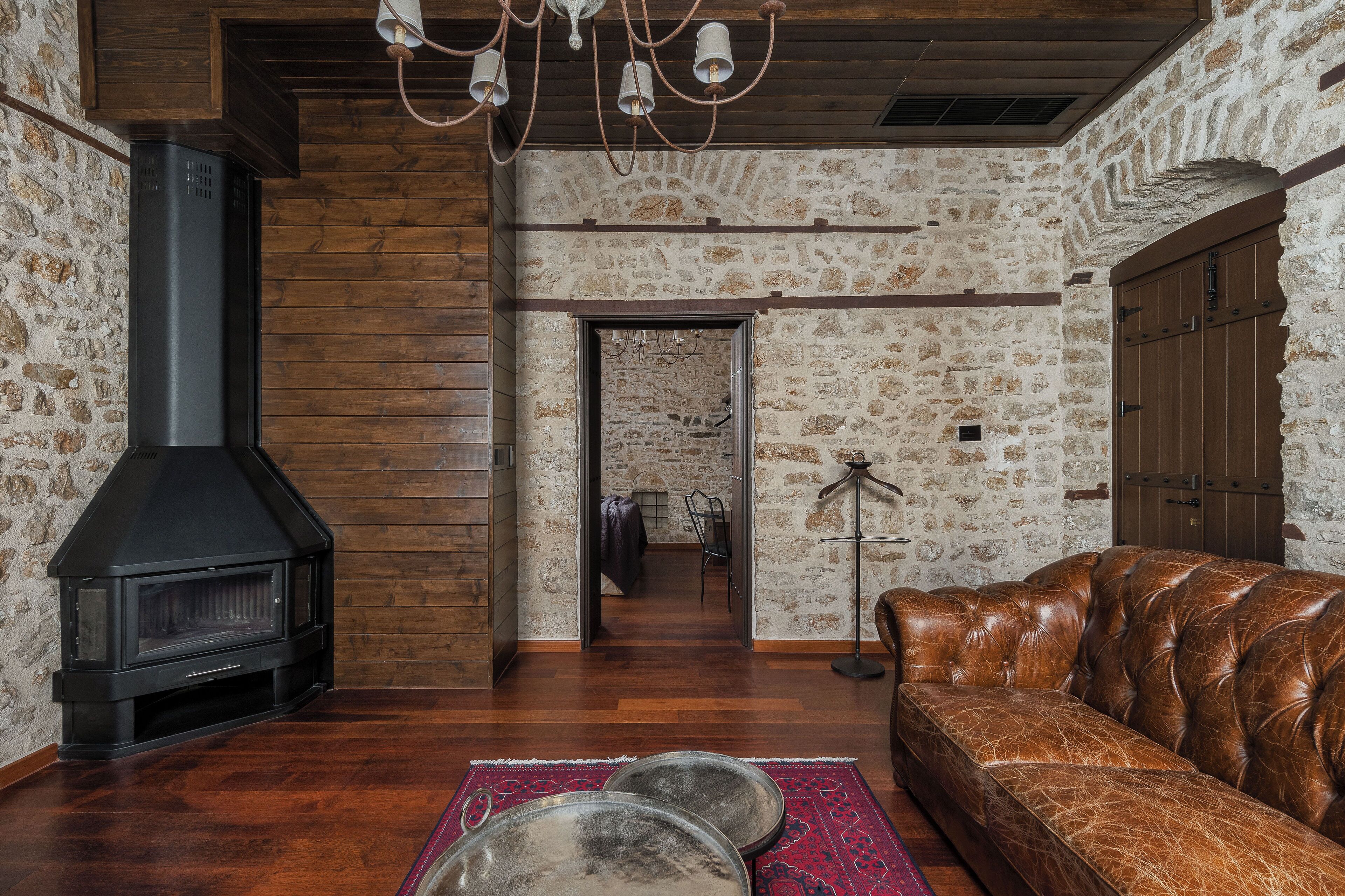 A cozy living room with a stone wall, a fireplace, a leather sofa, and a wooden ceiling.