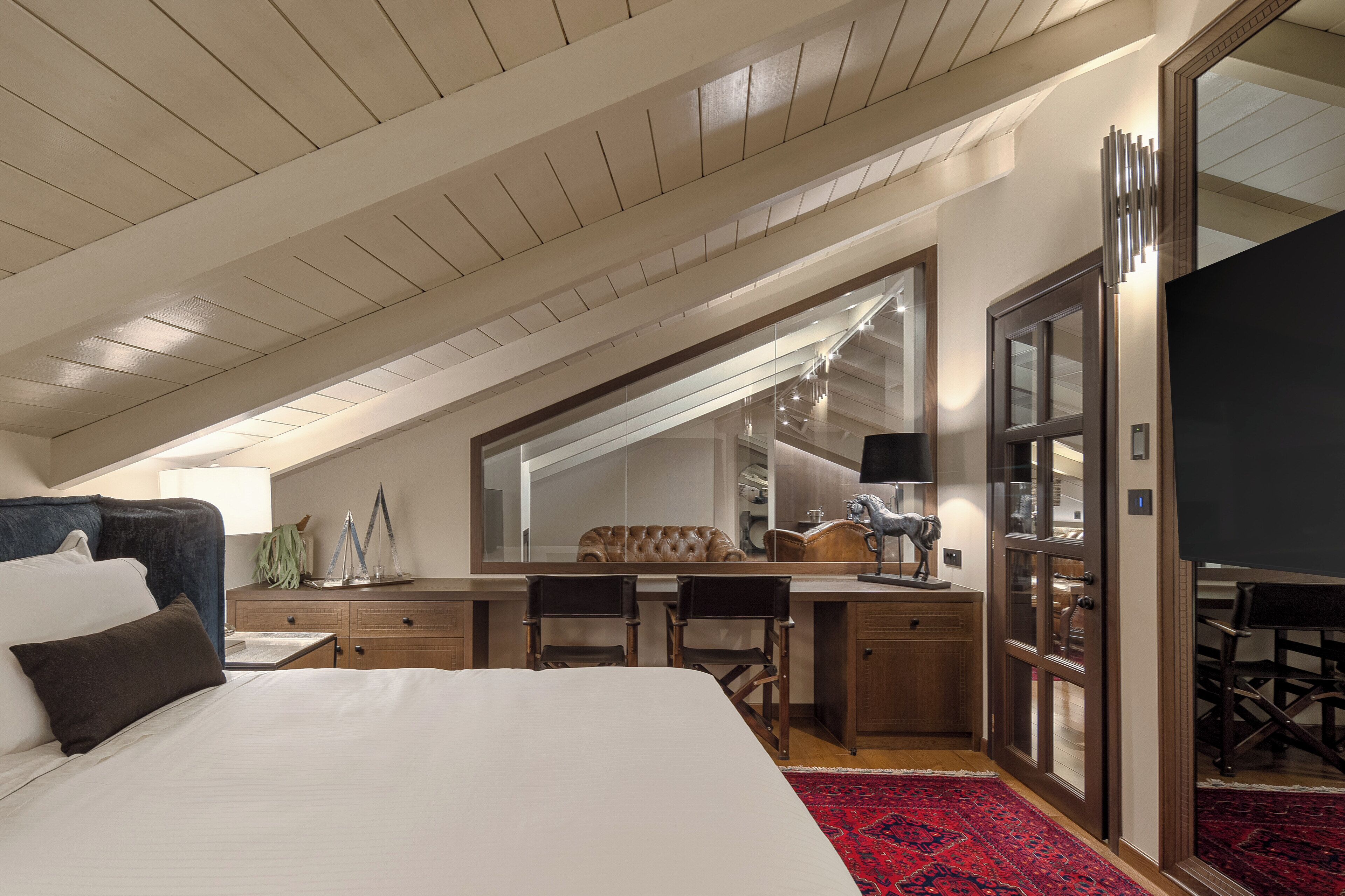 A hotel room with a large bed, a desk, two chairs, a mirror, and a red carpet.