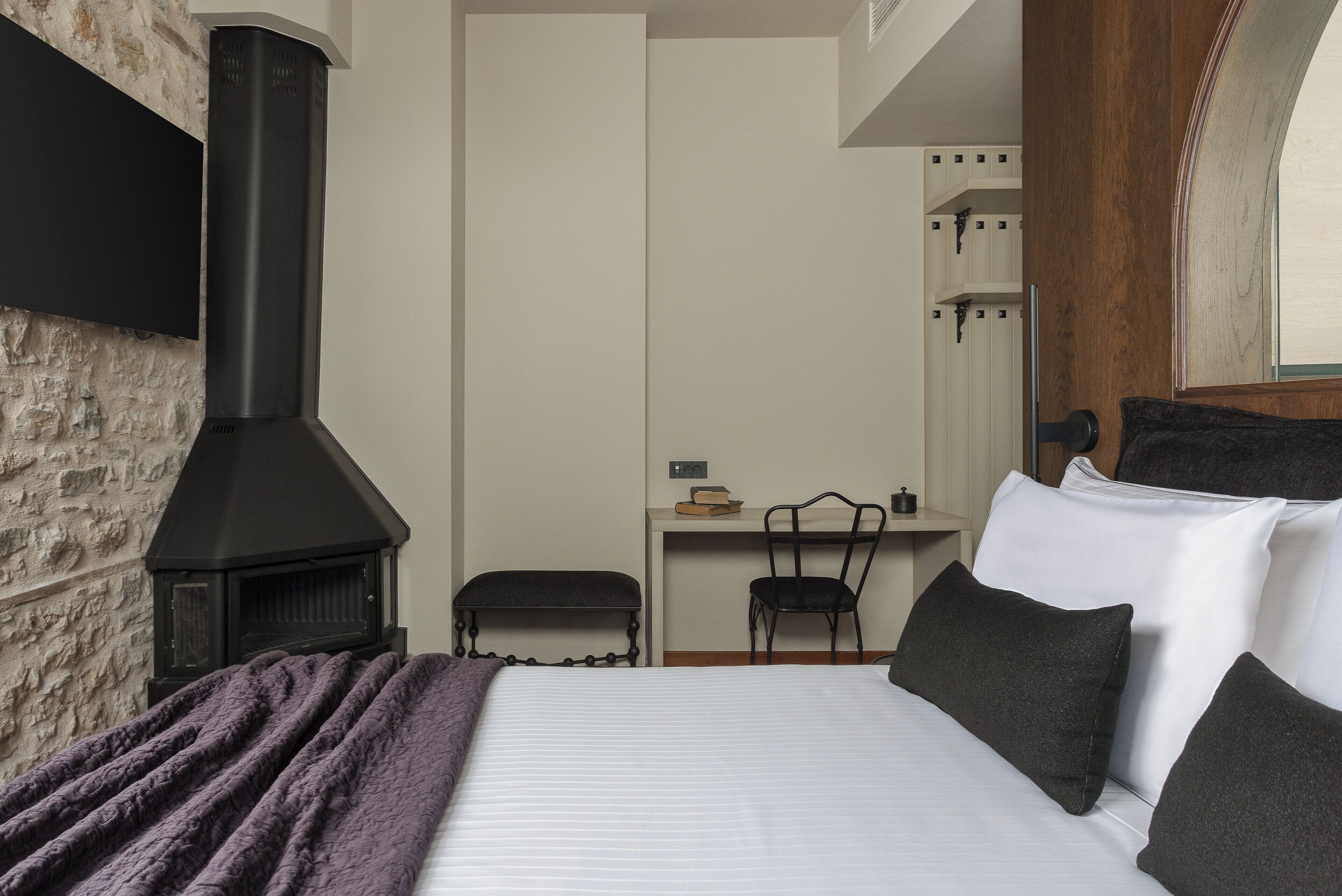 A bedroom with a bed, a bench, a desk, and a fireplace.