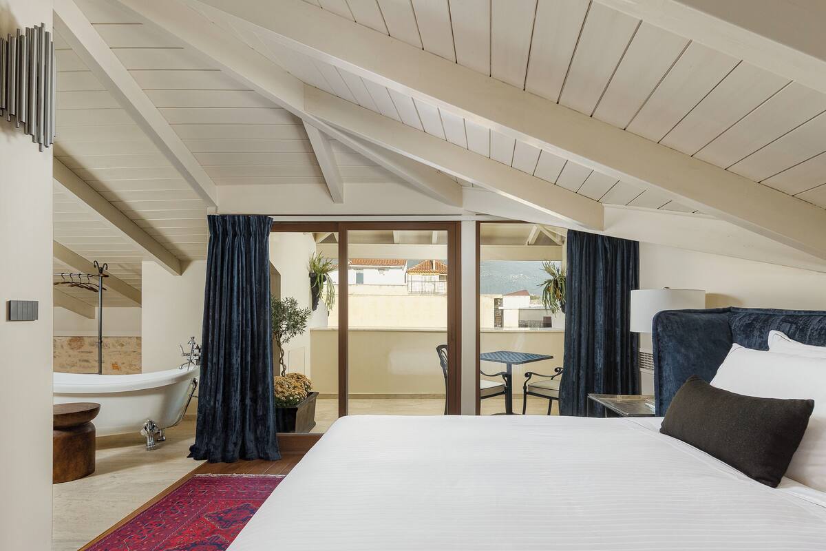 A bedroom with a large bed, a bathtub, a small table, and a chair.