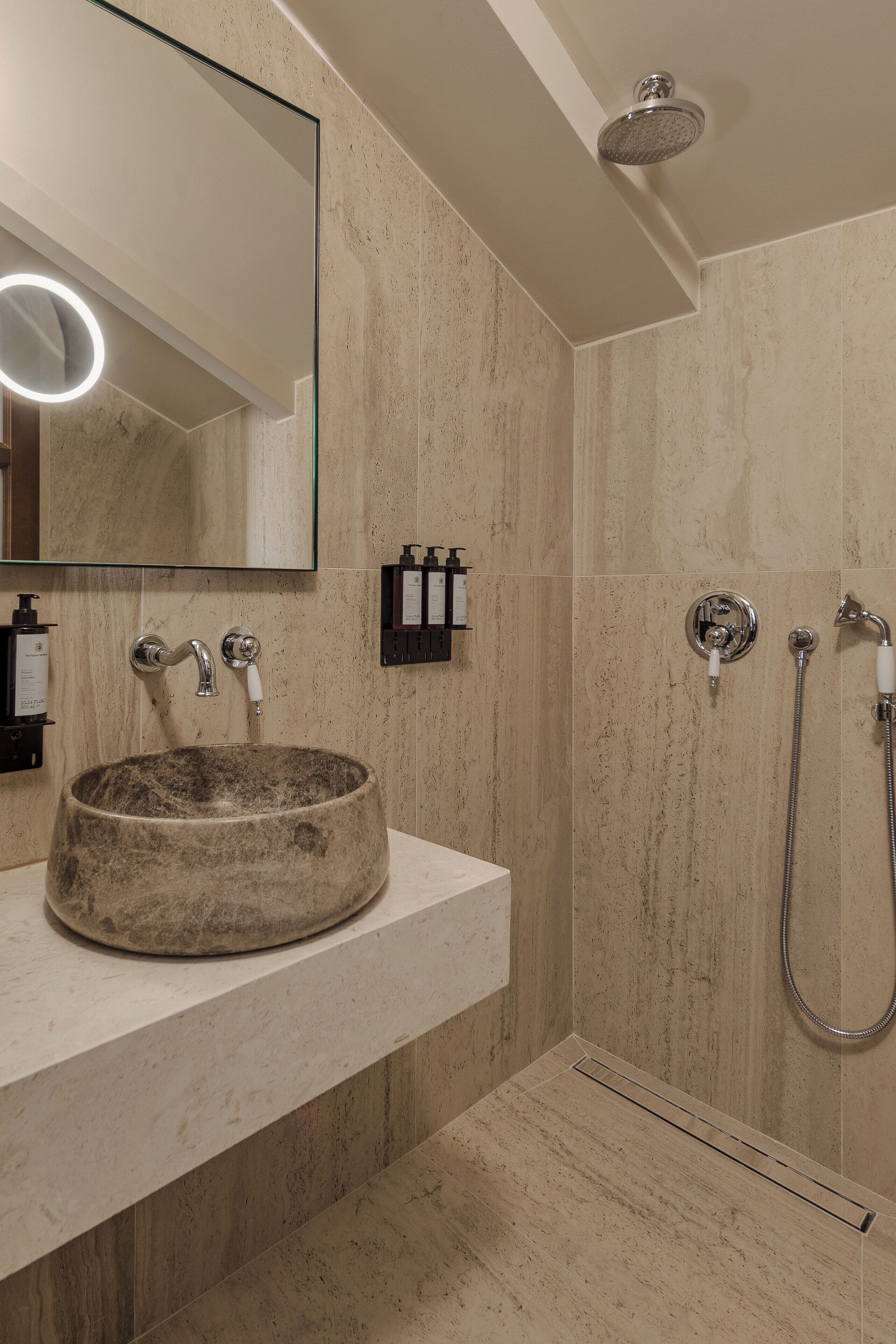 A bathroom with a round stone sink, a mirror, a shower, and a light fixture.