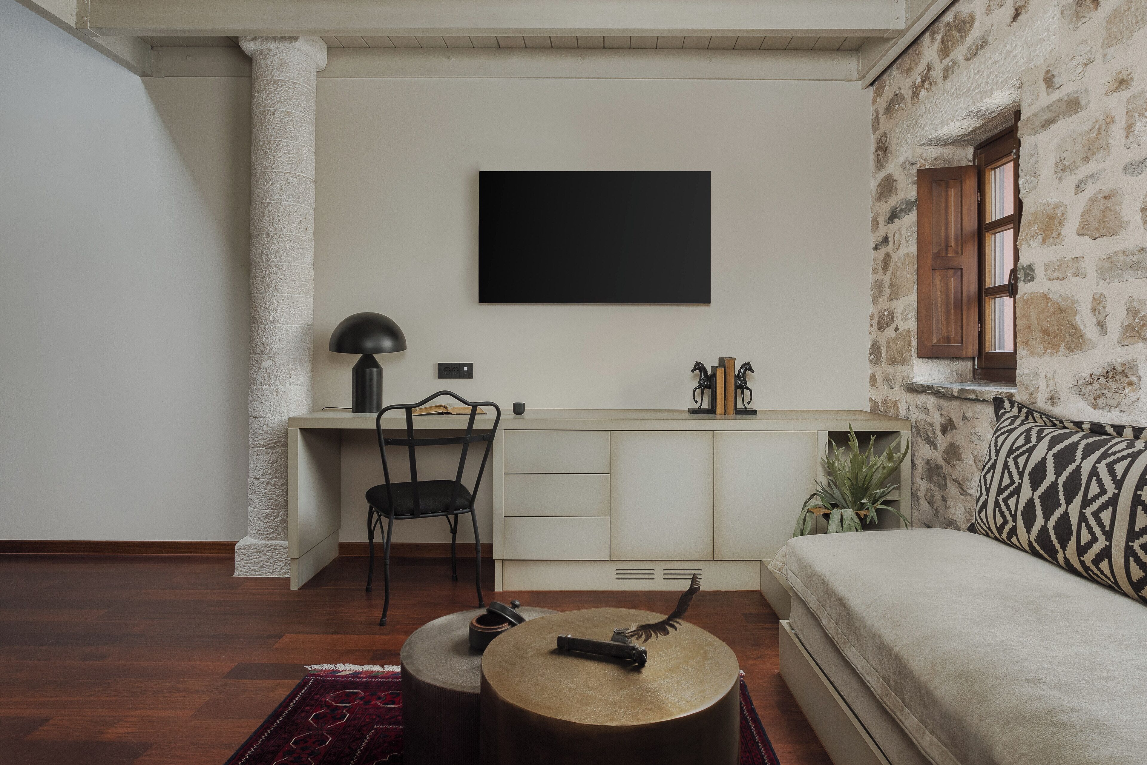 Una sala de estar moderna con un sofá, una mesa de centro, un escritorio con una silla y un televisor colgado en la pared.