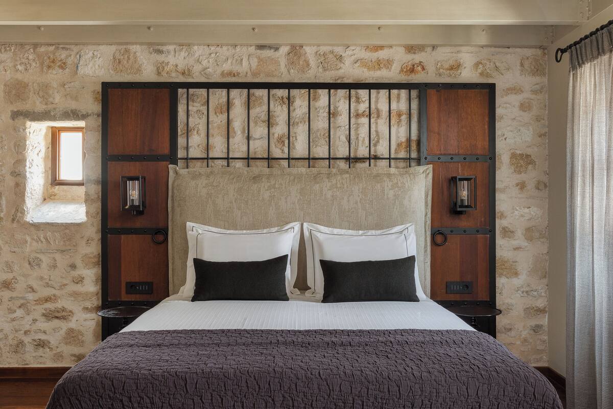 A bed with a headboard, two bedside tables, and a stone wall.
