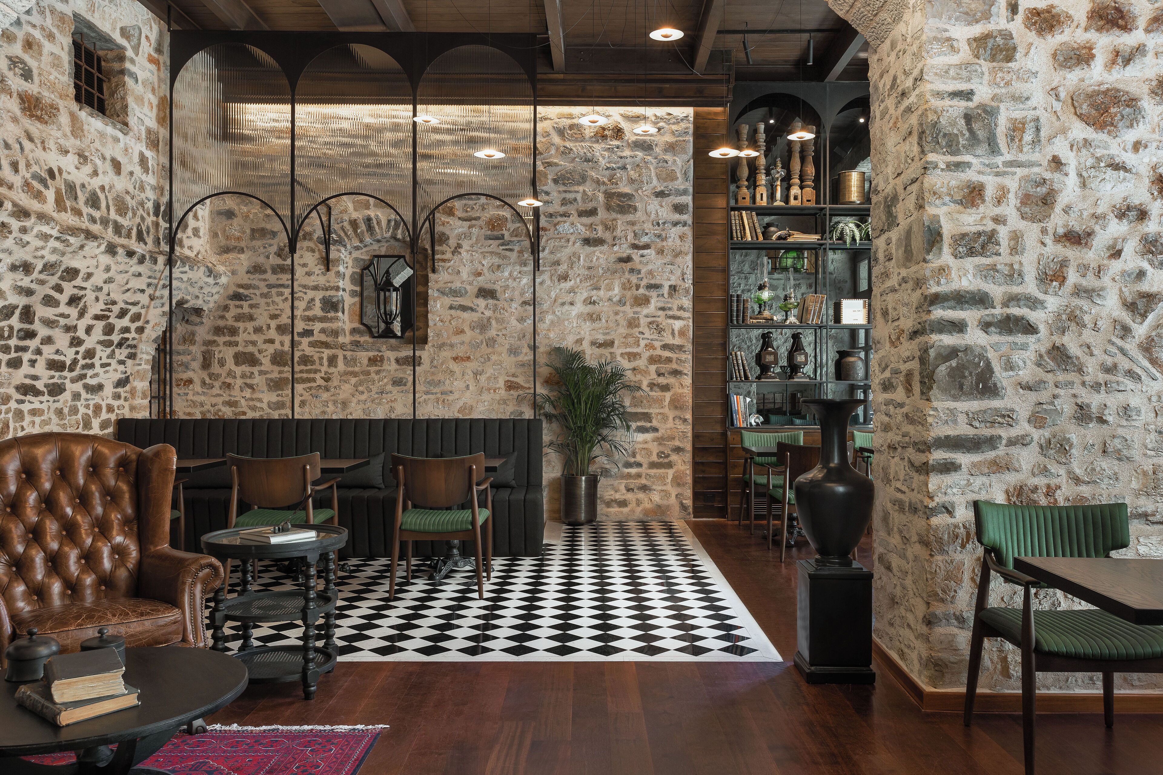 A cozy interior with stone walls, a checkered floor, and a mix of leather and green upholstered seating.