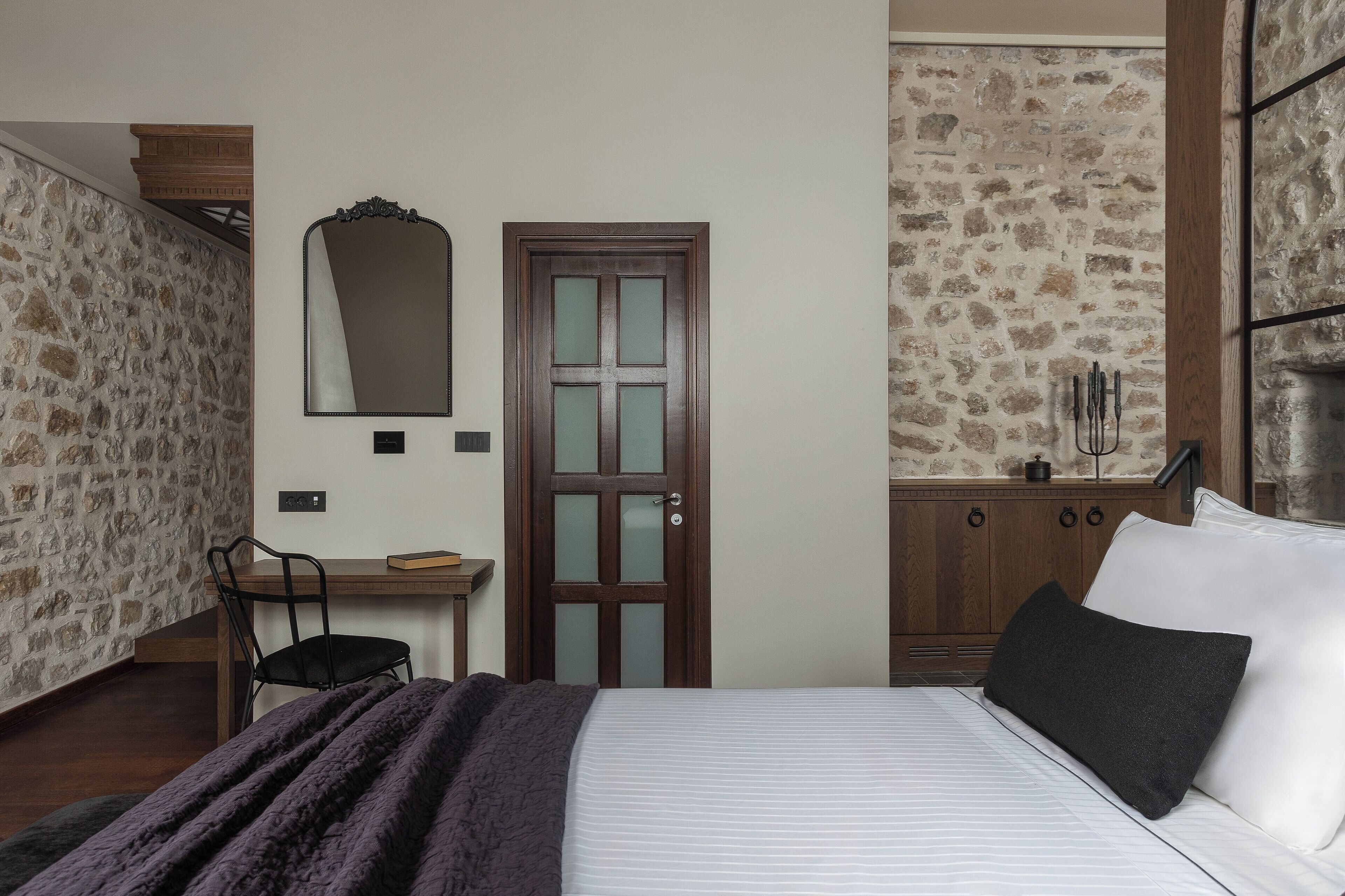 A bedroom with a bed, a desk, a chair, a mirror, and a door.