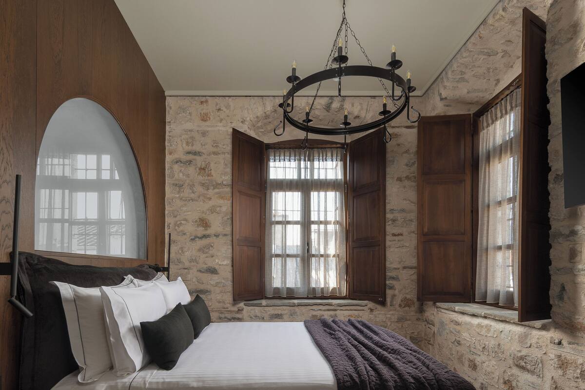 A bedroom with a large bed, wooden wardrobe, stone walls, and a chandelier.