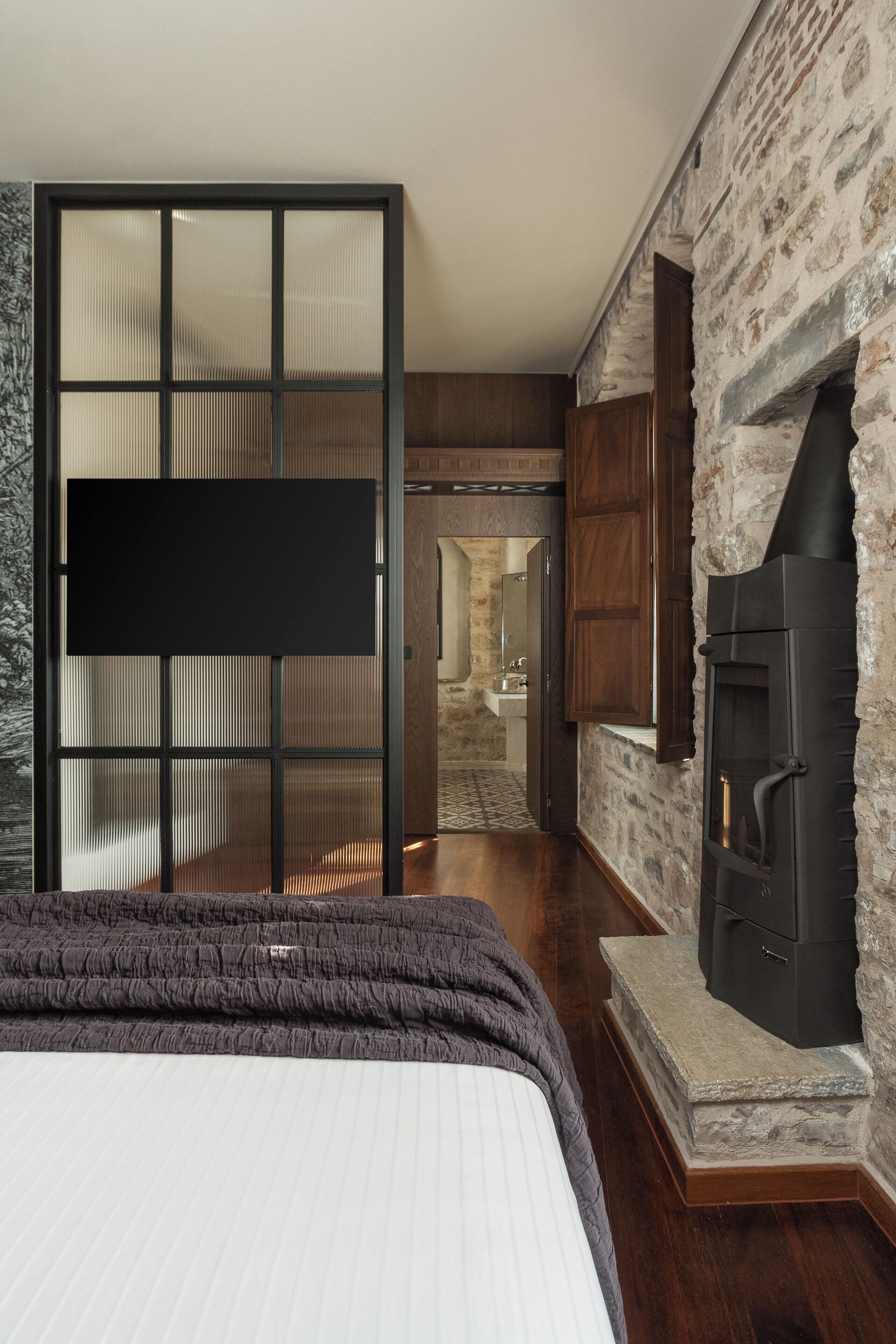 A bedroom with a bed, a TV, a stone wall, and a fireplace.