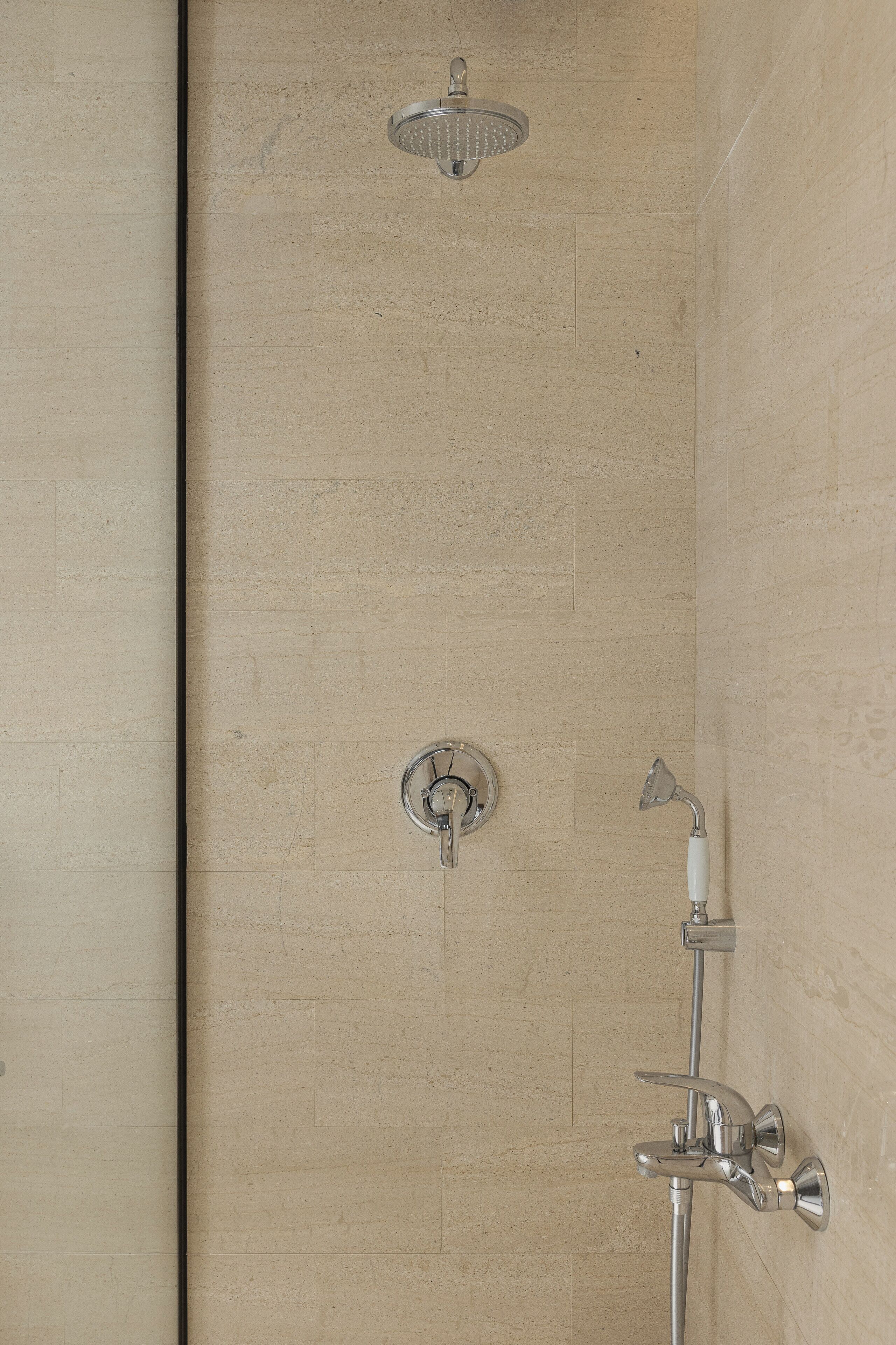 A shower with a handheld showerhead and a wall-mounted faucet.