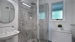 A modern bathroom with a glass shower enclosure, a white sink, and a window with frosted glass.