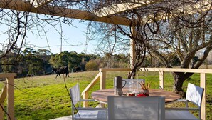 An outdoor dining area with a table and chairs under a pergola, overlooking a grassy field with cows in the distance. - The Cottage at Lake Werona (Werona)