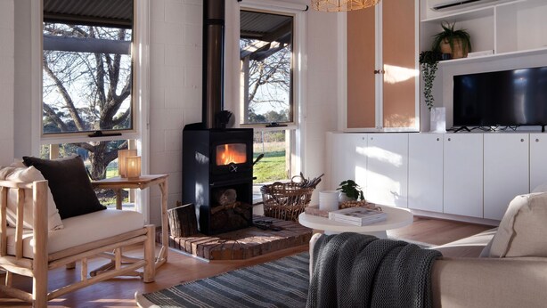 A cozy living room with a wood-burning stove, a television, and a view of the outdoors. - The Cottage at Lake Werona (Werona)