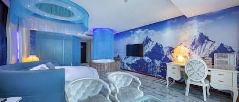 Un dormitorio moderno con una pared azul decorativa, un mural de montañas, una mesa de centro de vidrio y un aparador blanco.
