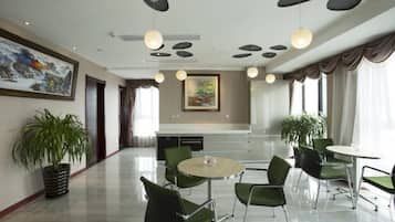 Espaço de refeições moderno em hotel, com mesa redonda, cadeiras verdes e iluminação pendente.