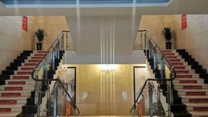 Un hall d’hôtel avec un escalier central, un lustre et des plantes en pot.