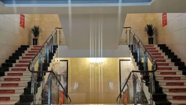 Un hall d’hôtel avec un escalier central, un lustre et des plantes en pot.