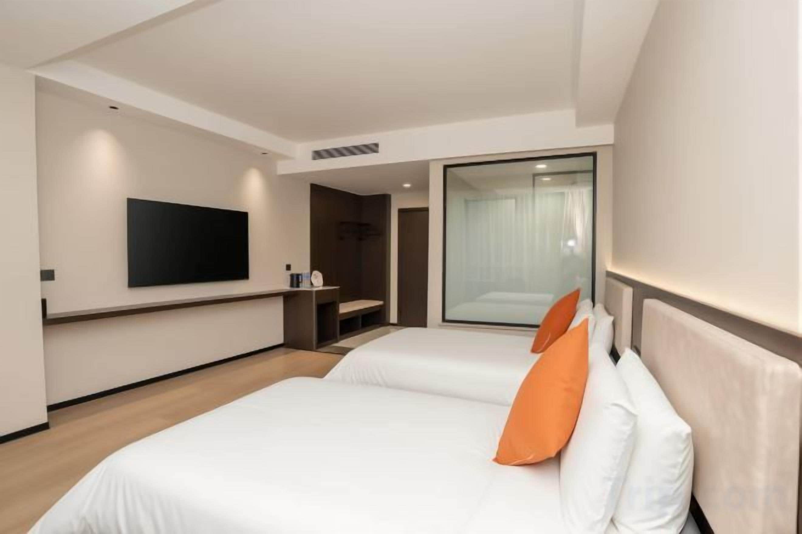Habitación de hotel con dos camas, un televisor de pantalla plana montado en la pared y una puerta corrediza de vidrio que da a un balcón.