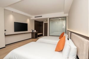 Habitación de hotel con dos camas, un televisor de pantalla plana montado en la pared y una puerta corrediza de vidrio que da a un balcón.