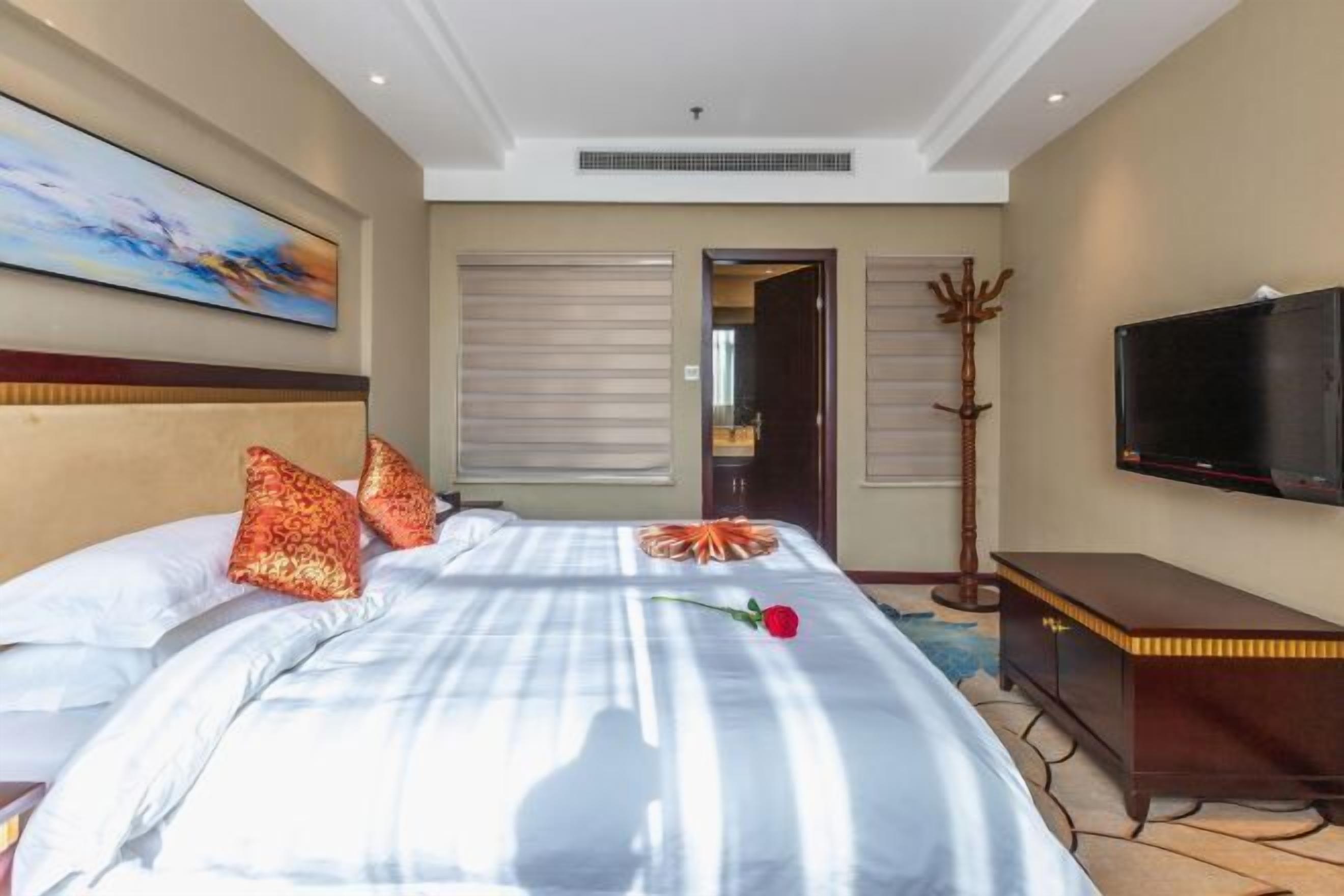 A hotel room with a bed, a television, and a painting on the wall.