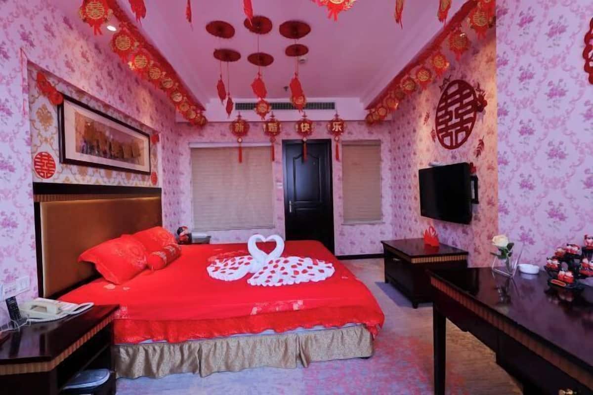 Habitación de hotel con cama, mesita de noche, televisión y un adorno en la pared.