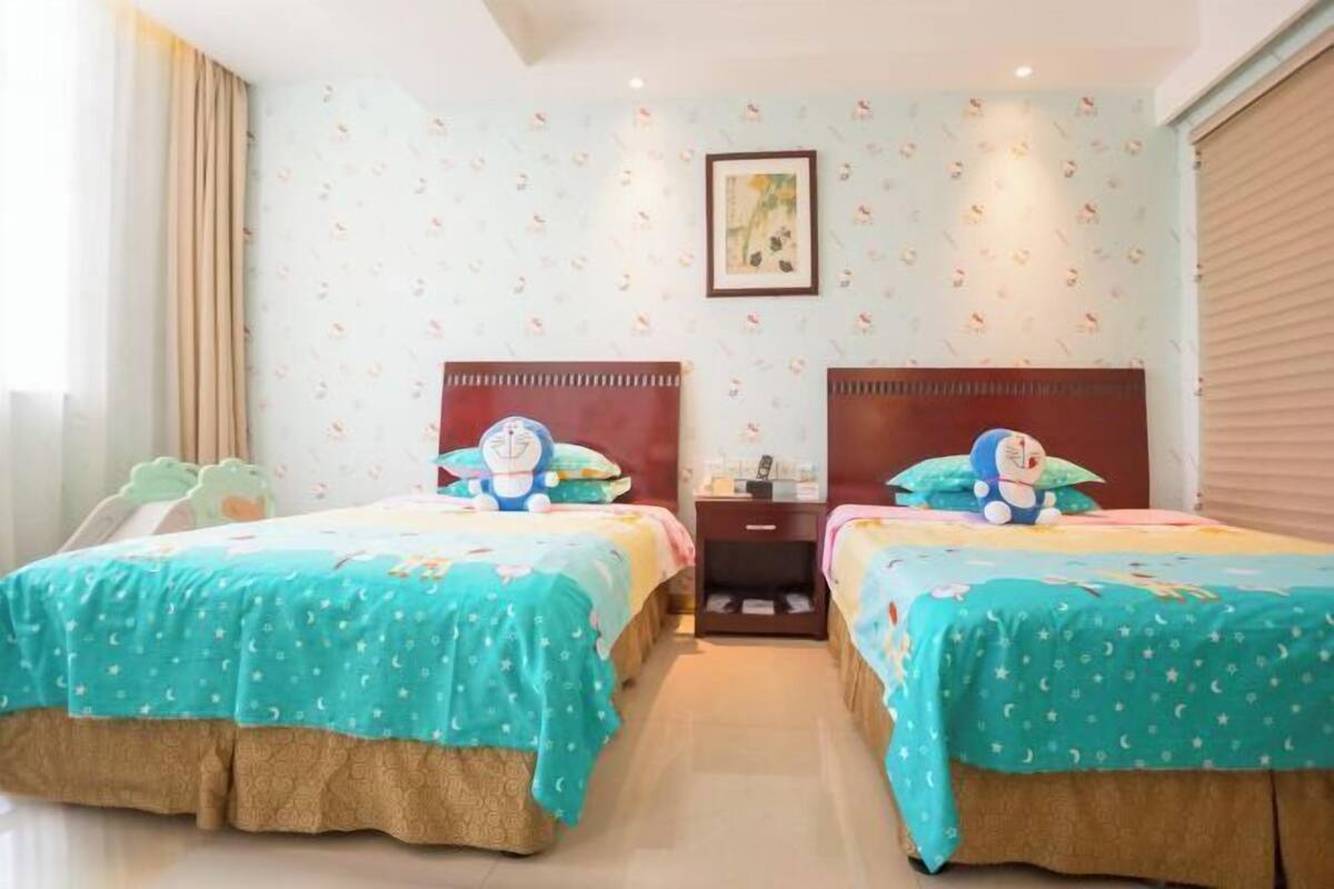 Habitación de hotel con dos camas, una mesita de noche, una lámpara y un ventanal con cortinas.
