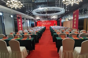 Un salón de conferencias con filas de mesas y sillas, una alfombra roja y un escenario con un cartel.