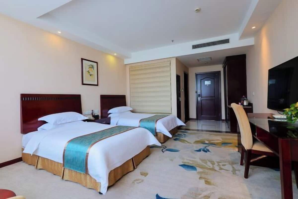 Habitación de hotel con dos camas, un escritorio, una silla, un televisor y una puerta que da a un baño.