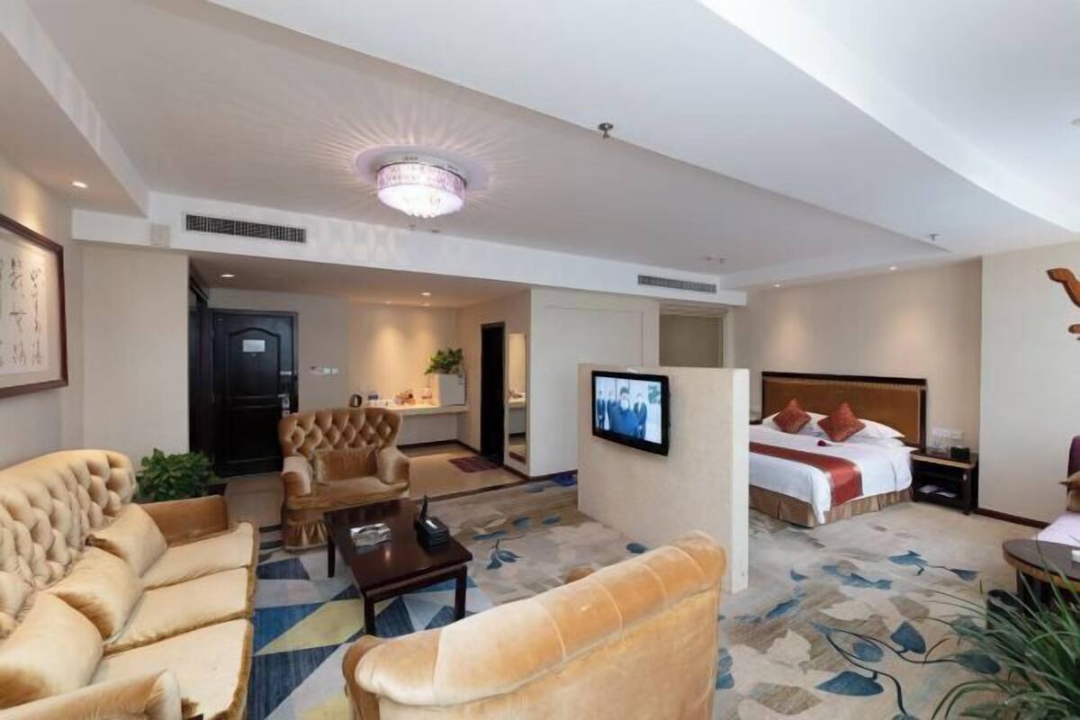 Una habitación de hotel con una cama grande, televisión, sofá y sillón.