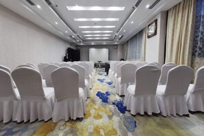 A conference room with rows of white chairs, a carpet with a floral pattern, and a projector screen at the front. - Huixian Shangquan Yipin Hotel (Huixian)