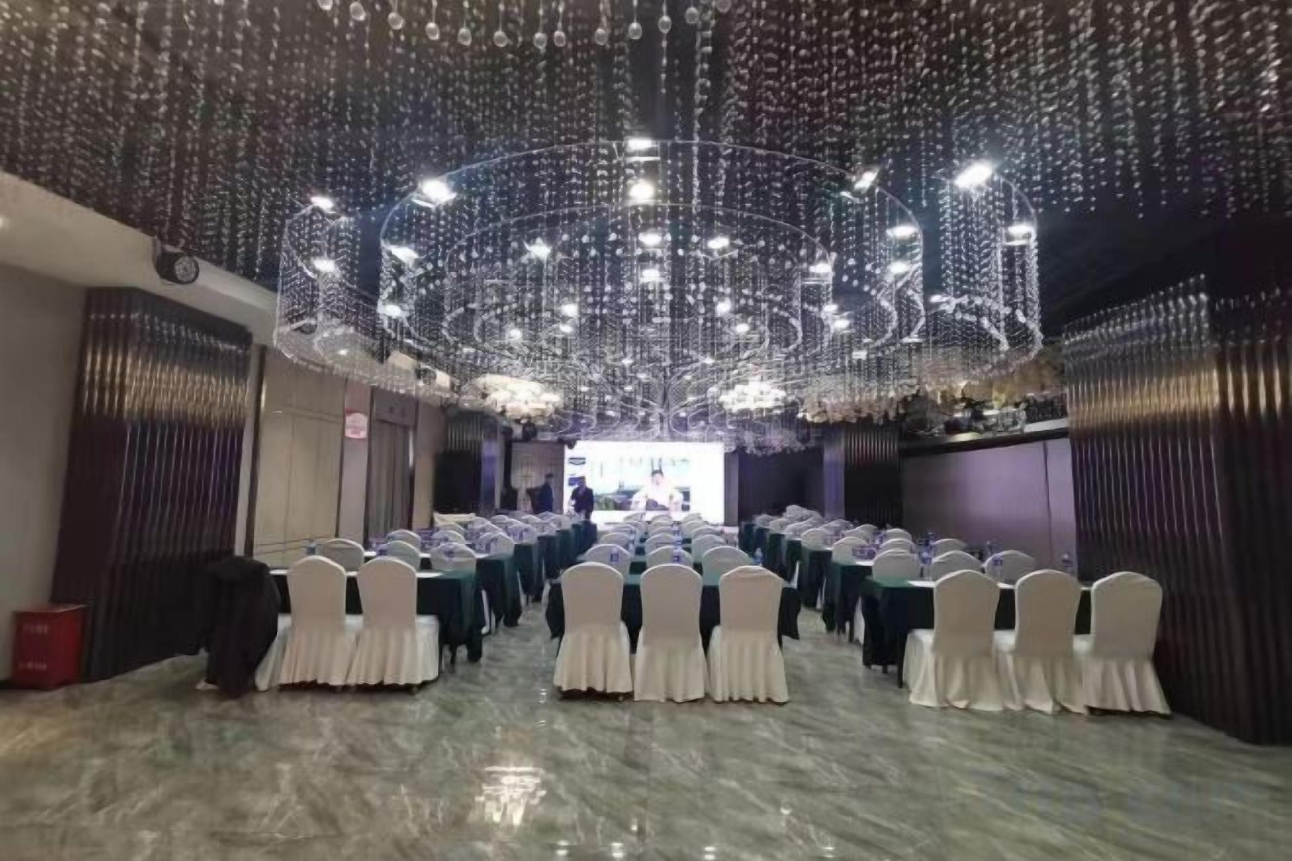 A banquet hall with rows of tables and chairs, a chandelier, and a stage.