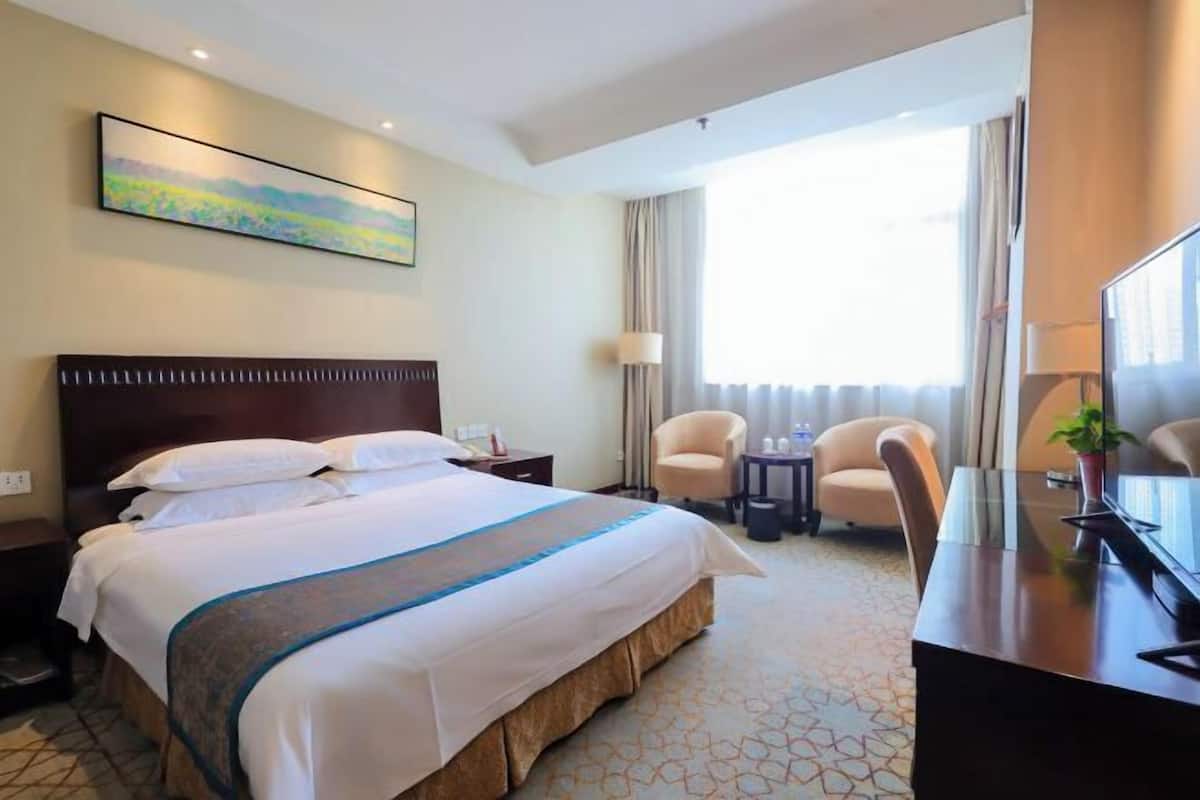 Habitación de hotel con una cama grande, un escritorio, una silla, un televisor y una ventana con cortinas.