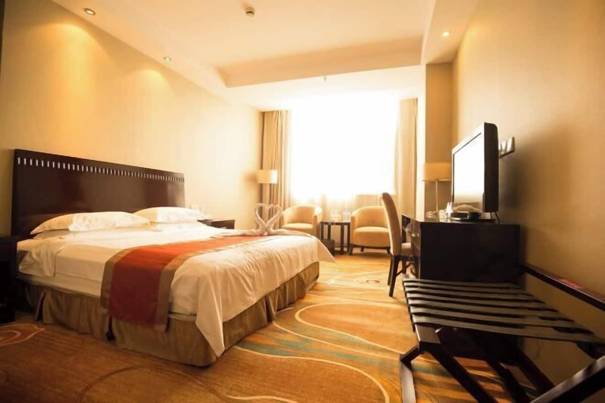 Una habitación de hotel con una cama grande, un escritorio con una silla, un televisor y una ventana con cortinas.