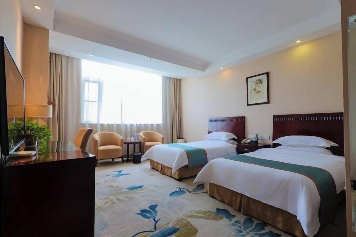 Habitación de hotel con dos camas, un escritorio, una silla, una mesita y una ventana con cortinas.