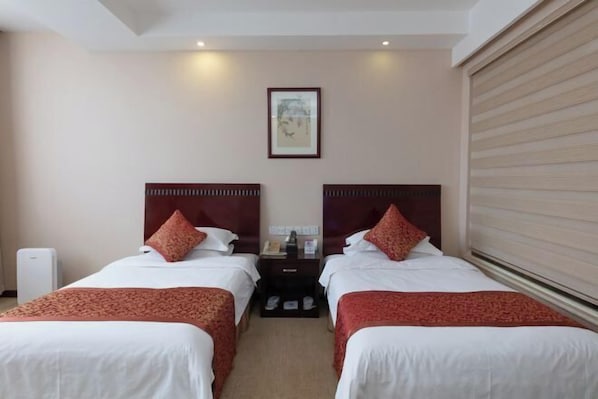 A hotel room with two beds, a nightstand, a framed picture on the wall, and a window with blinds.