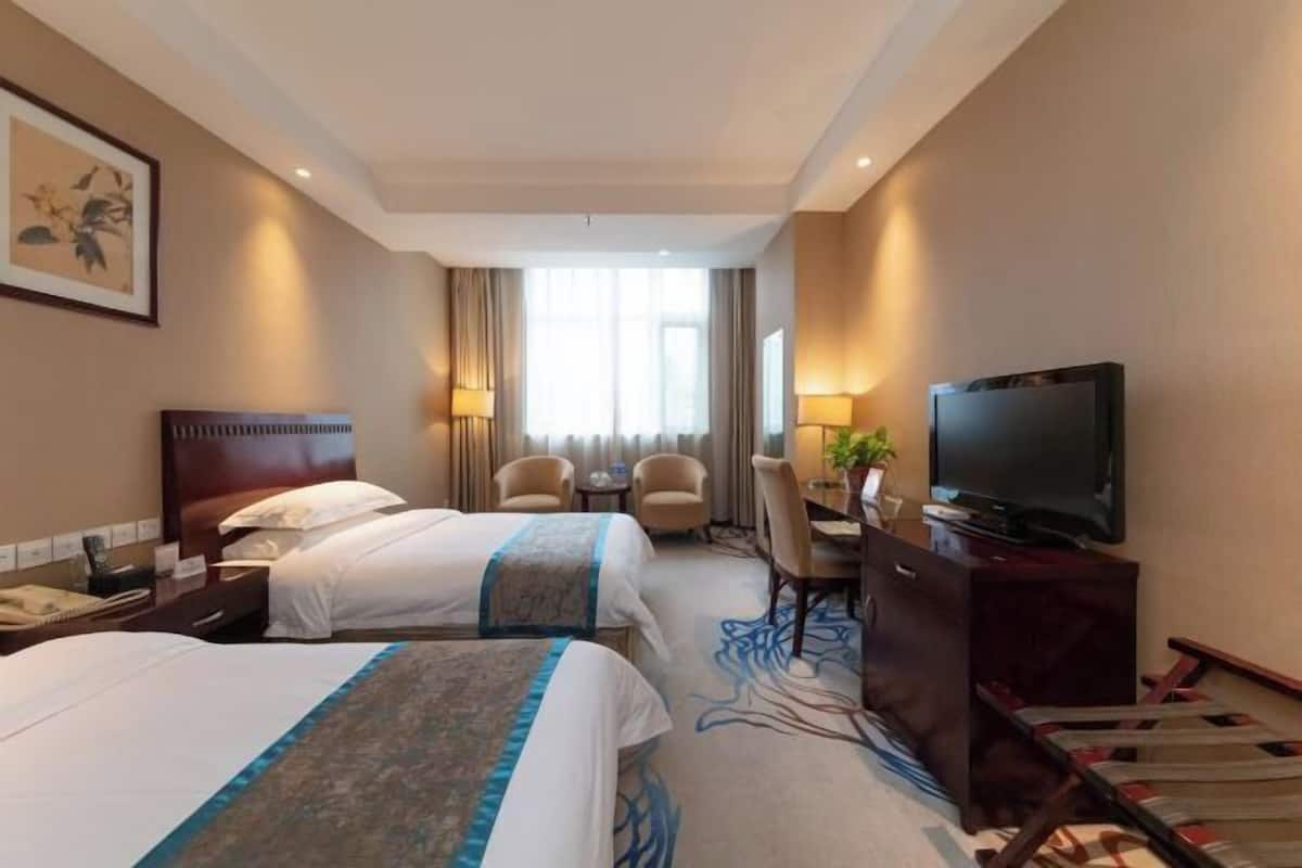 Habitación de hotel con dos camas, un escritorio, un televisor y un cuadro en la pared.