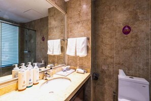 Un bagno con uno specchio grande, due asciugamani bianchi appesi al muro, un lavandino con articoli da toilette e un box doccia.