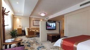 Une chambre d’hôtel comprenant un lit, une télévision, un coin salon avec un canapé et des fauteuils, une petite table et une plante en pot.