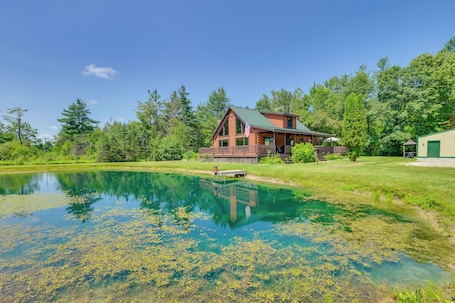 A lodge with a large pond, surrounded by trees and a clear sky.