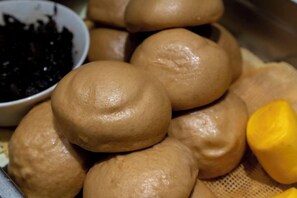 A stack of round, brown baked goods with a smooth surface, possibly bread or buns, and a bowl of dark-colored food in the background. - Jundu Boutique Hotel (Jinhua Stadium) (Jinhua)