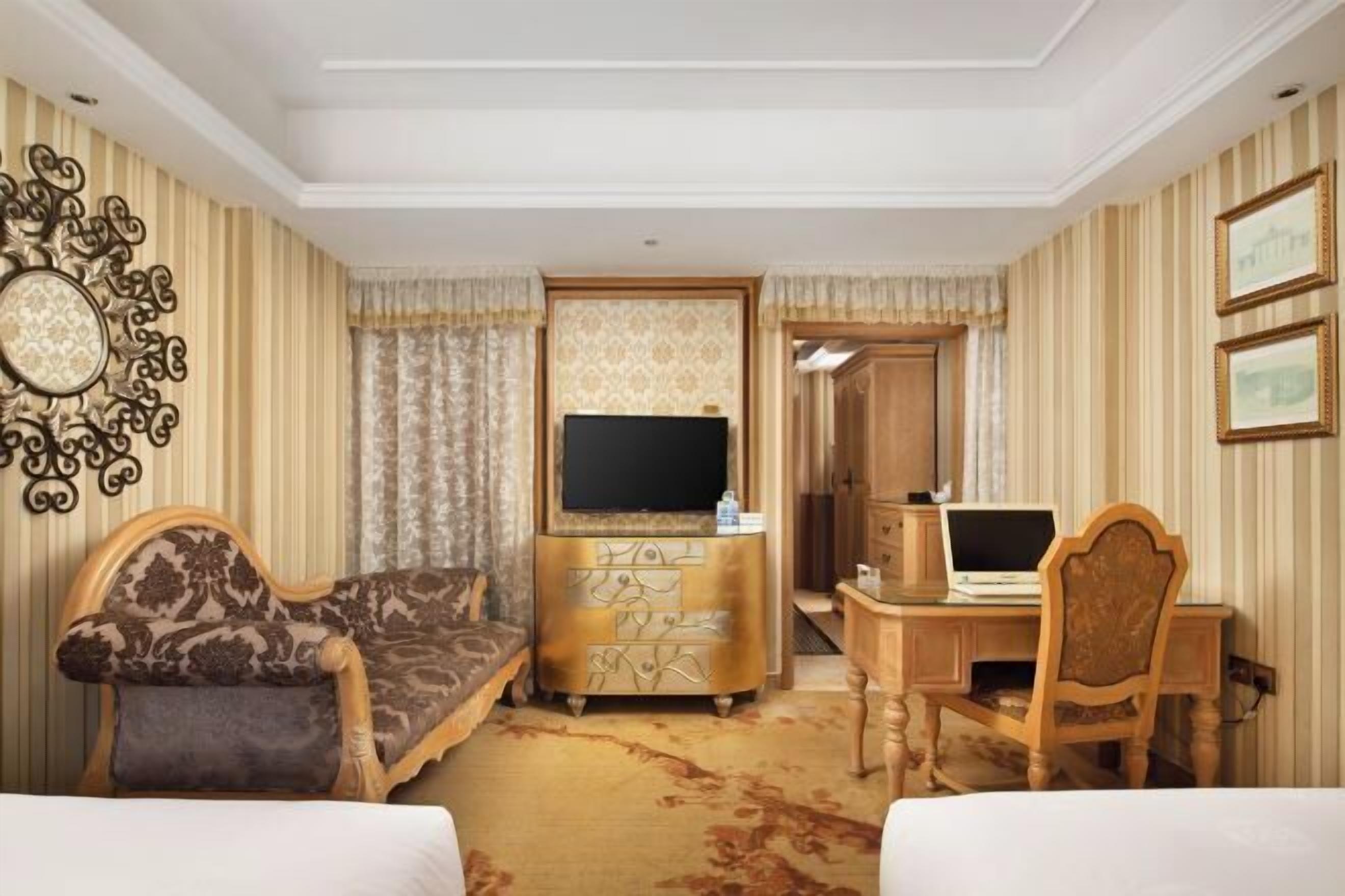 A hotel room with a sofa, a TV, a desk with a computer, and a bed.