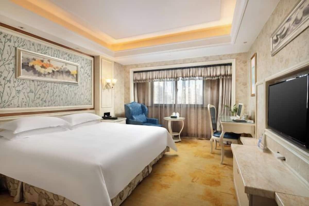 Une chambre d’hôtel avec un lit, un bureau avec un ordinateur, une chaise, une télévision et une fenêtre avec des rideaux.