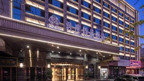 Hotel com vários andares, entrada imponente com toldo e sinalização iluminada.