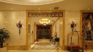 Um saguão de hotel com piso estampado, um lustre, arandelas e um balcão de recepção.