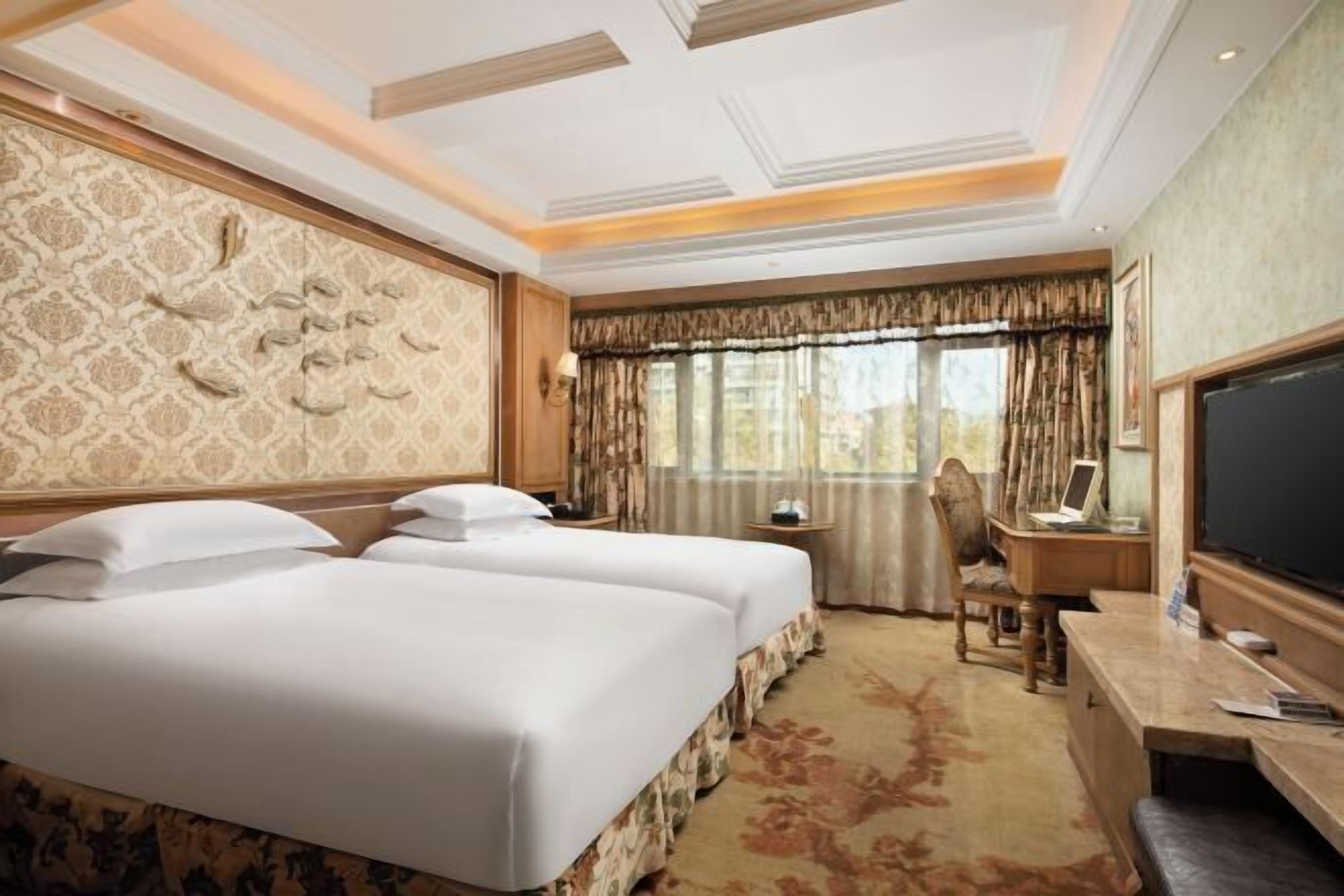A hotel room with two beds, a desk, a chair, a television, and a large window with curtains.