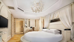Um quarto luxuoso com uma cama redonda, um candelabro e uma janela grande com cortinas.