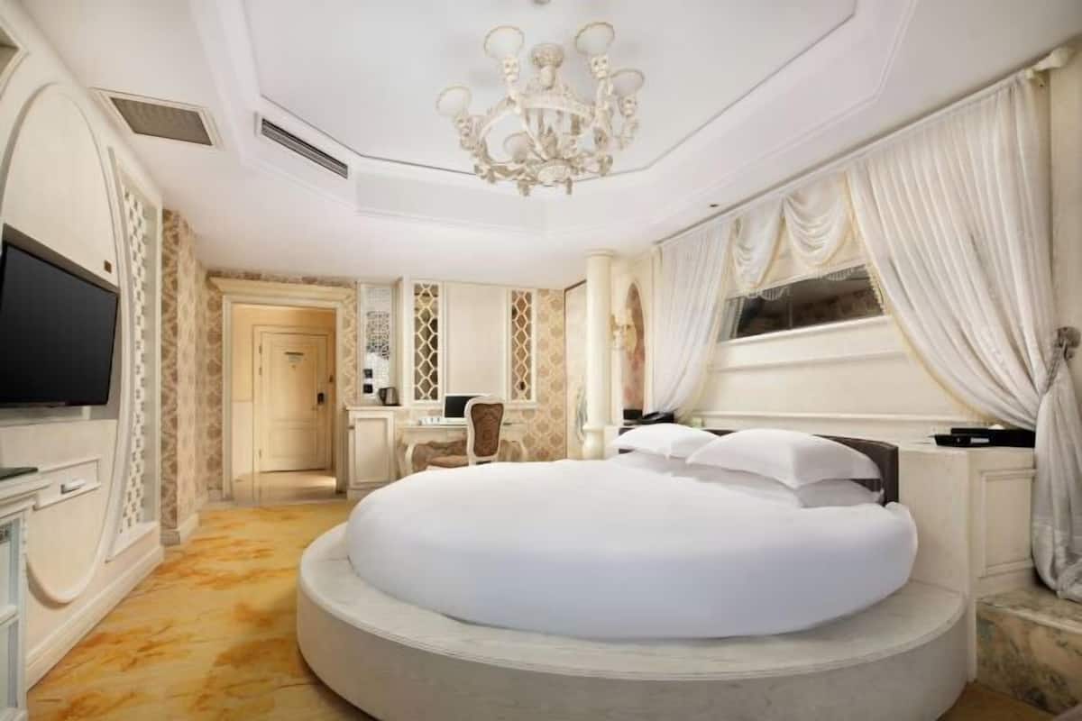 Une chambre à coucher luxueuse avec un lit rond, un lustre et une grande fenêtre avec des rideaux.