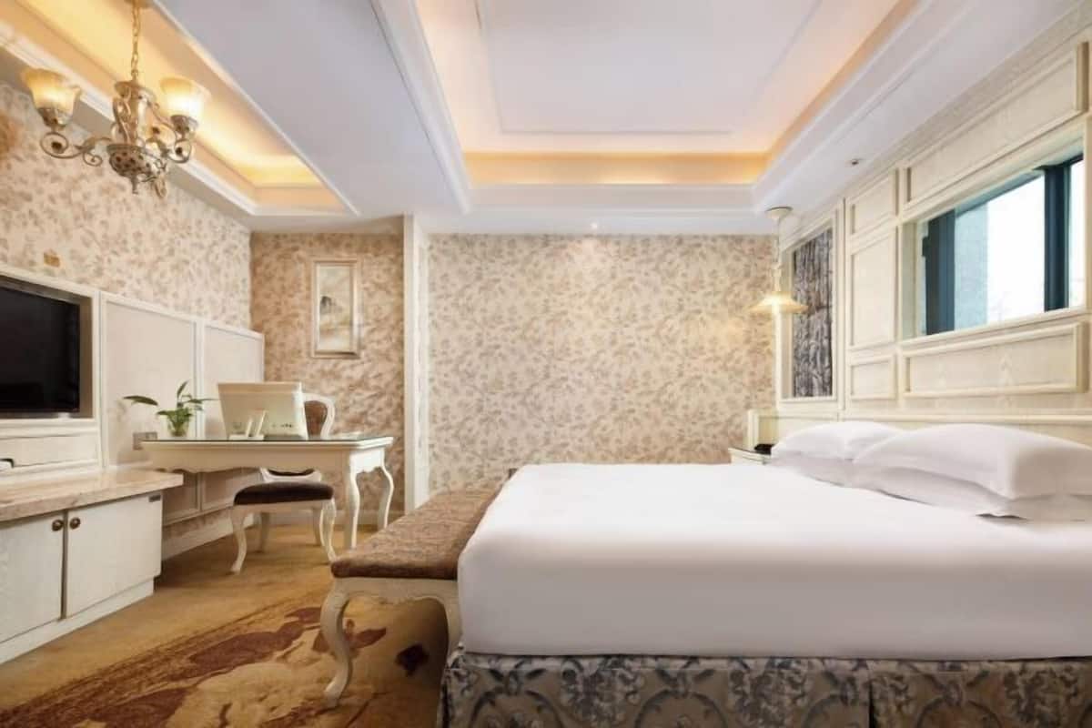 Une chambre d’hôtel avec un lit, un bureau, une télévision et un lustre.