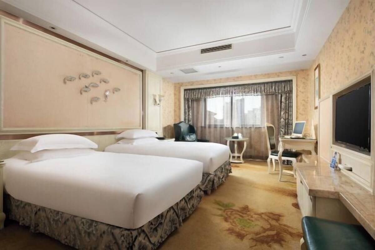 Une chambre d’hôtel avec deux lits, un bureau, une télévision et une fenêtre avec des rideaux.